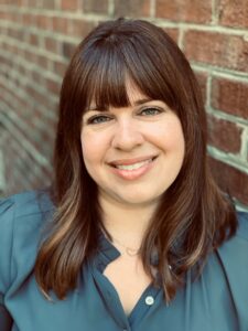 Erin Steam Headshot. She has brown hair at shoulder length and wearing a green blouse.